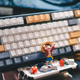 An image of a custom keyboard with a toy of Luffy from One Piece cheering in front.